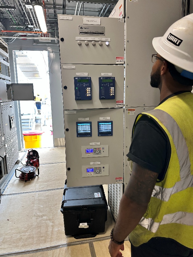 A technician reviews protective relays and control devices in an electrical equipment lineup.