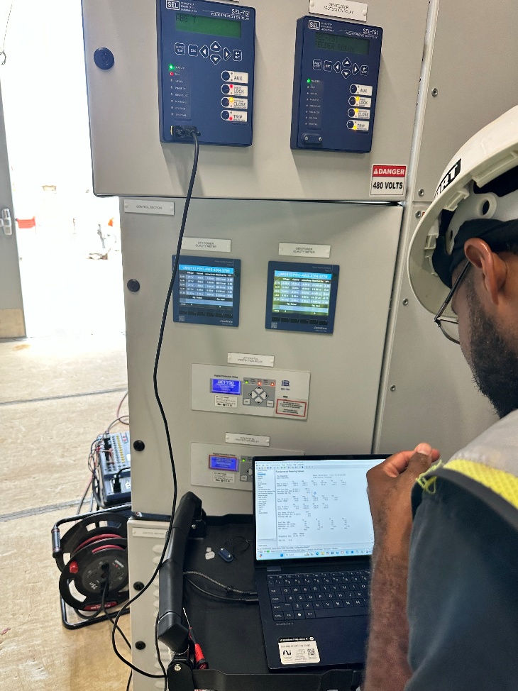 A technician reviews relay test software beside a protection and control lineup.
